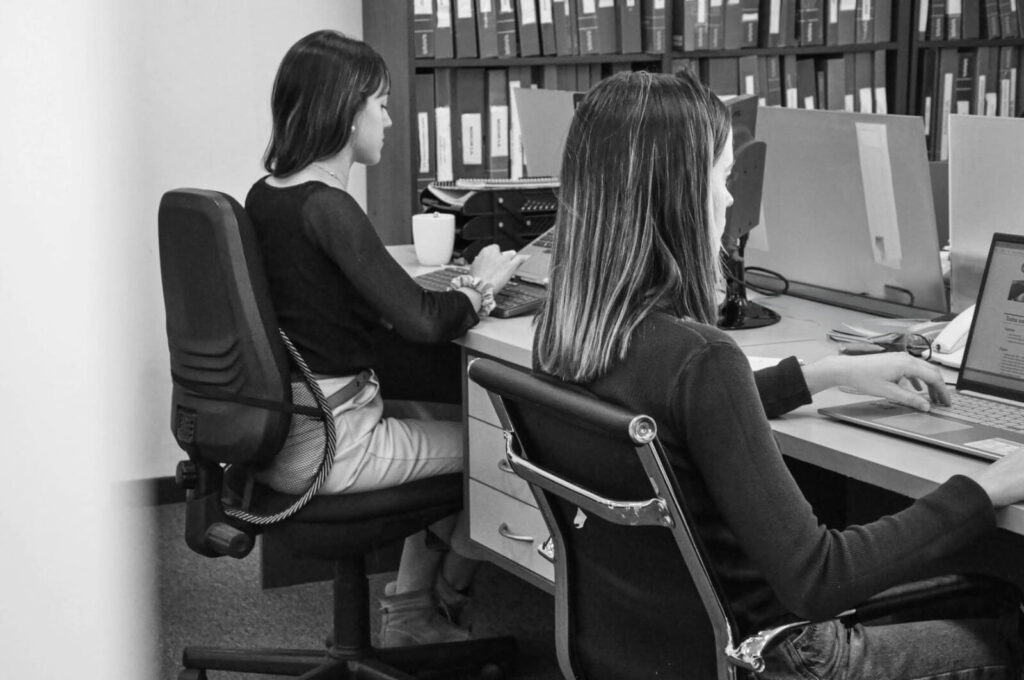 Equipo dos mujeres sentadas en una oficina trabajando frente a una computadora